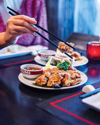 A plated Japanese dish being lifted with chopsticks at a table on board