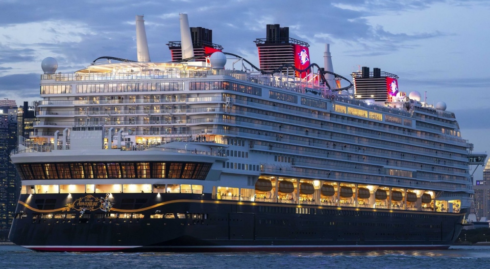 Disney Adventure at dusk, her funnels lit, a city skyline behind her