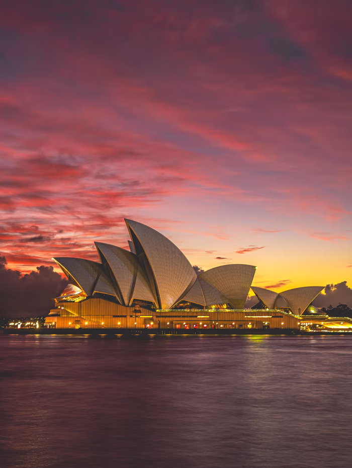 Sydney Opera House lit at sunset across the harbour